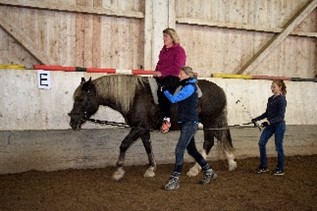 Eine Patientin sitzt auf einem Pferd und wird von den Therapeutinnen geführt